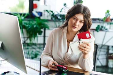 A young beautiful plus size woman examines her financial documents thoughtfully at office. clipart