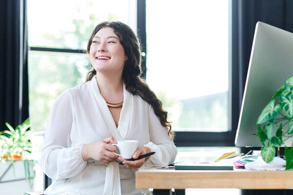 The young woman relaxes at office, savoring coffee and basking in natural light.