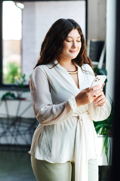 Женщина plus size трезво улыбается, прокручивая свой телефон в ярком, уютном офисном пространстве.