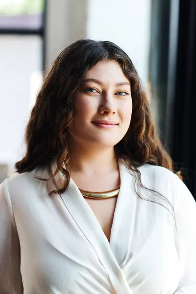 stock image A young woman with curly hair radiates confidence and warmth in her stylish office setting.