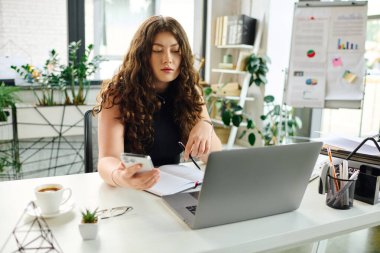 Kendine güvenen genç bir profesyonel, modern ofis masasındaki notları incelerken akıllı telefonuyla meşgul oluyor..