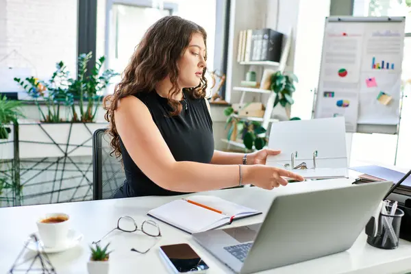 stock image A confident businesswoman efficiently organizes documents while seated at her desk, immersed in her work.