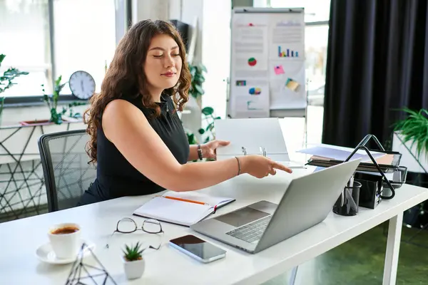 stock image A young professional woman collaborates at her modern desk, showcasing her expertise in a vibrant office environment.