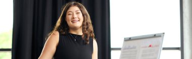 Uzun kıvırcık saçlı, kendine güvenen genç bir kadın meslektaşlarını coşkuyla parlak bir ofis ortamında meşgul ediyor..
