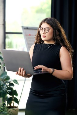 Büyük beden kıvırcık saçlı bir iş kadını laptopuna odaklanmış, kurumsal görevlerine dalmış, kendini adamışlığını sergiliyor..