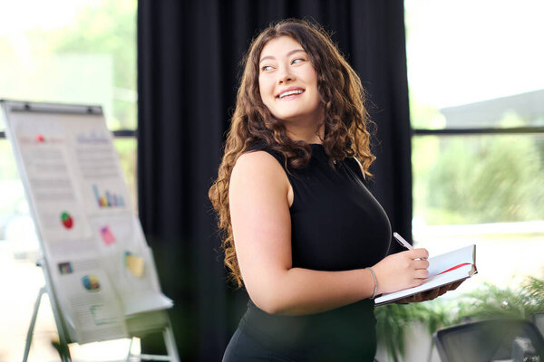 Уверенная женщина с длинными вьющимися волосами старательно пишет заметки в стильной офисной обстановке, воплощающей корпоративную культуру.