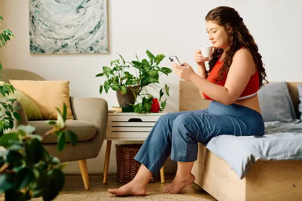 stock image A beautiful plus size woman relaxes at home, sipping her tea while scrolling through her phone in a cozy atmosphere.