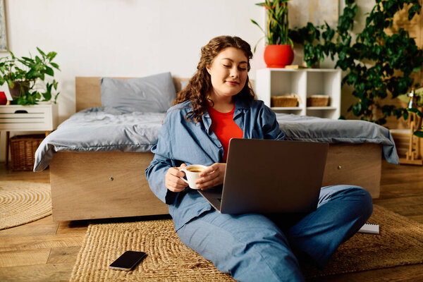 Потягивая кофе и фокусируясь на своем ноутбуке, красивая молодая женщина создает уютную атмосферу в своем доме.