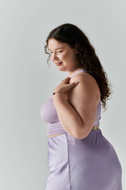 A plus size woman smiles gently in a lavender outfit against a neutral background. clipart