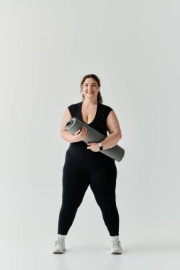 Güzel, iri yarı bir kadın elinde yoga minderiyle gururla duruyor. Zarafet ve güven saçıyor..