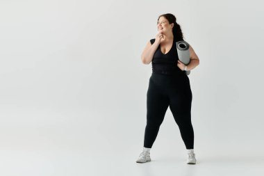 A confident plus size woman stands with a yoga mat, smiling in a bright, minimalistic room. clipart