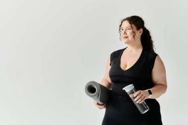 Kendine güvenen, güzel ve iri yarı bir kadın yoga minderi ve su şişesiyle antrenmana hazır bekliyor..