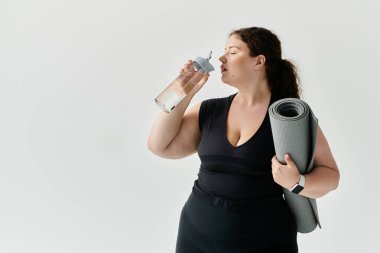 Kendine güvenen iri yarı bir kadın yoga minderini tutarken ferahlatıcı bir içkiden hoşlanır..