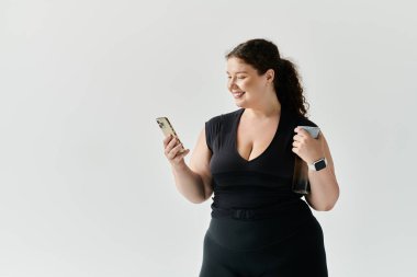 A beautiful plus size woman smiles while using her phone in a chic, minimalist space. clipart