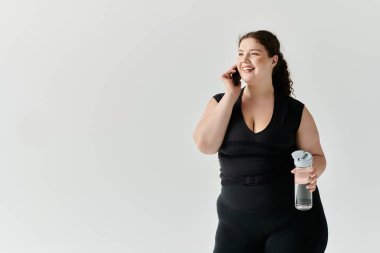 Şık, iri yarı bir kadın, elinde su şişesi tutarken telefonla sohbet ederken ışıl ışıl gülümser..