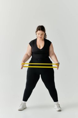 An elegant plus size woman strengthens her body using resistance bands in a sleek studio. clipart