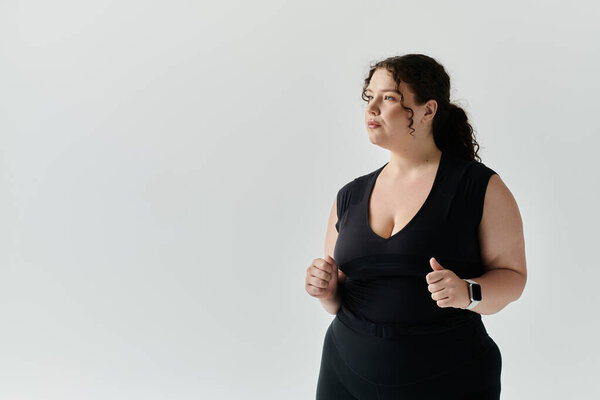A graceful plus size woman stands confidently, showcasing her elegance in a simple studio.