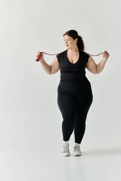 Изящный плюс размер женщина позирует с скакалкой, источая уверенность и силу.