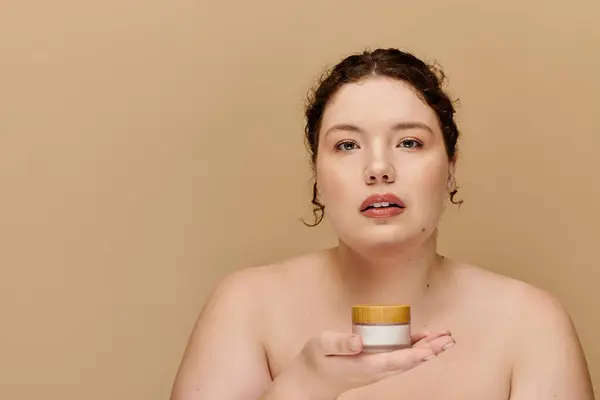 stock image A confident plus size woman presents a skincare product, embracing natural beauty and self care.