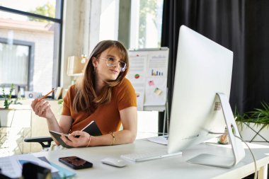 Genç ikili olmayan birey parlak bir ofis çalışma alanında otururken fikirleri yansıtır..