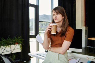 In a contemporary workspace, a non binary individual ponders over notes while savoring coffee. clipart