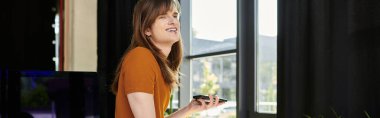 A non binary youth smiles while using their smartphone in a lively office. clipart