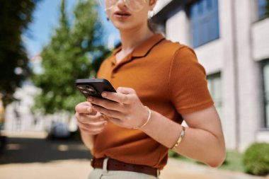 Çevresi yeşillik ve modern mimari ile çevriliyken bir birey akıllı telefonuyla meşgul olur..