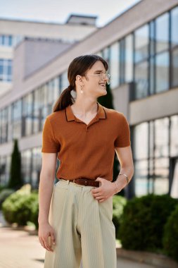 Neşeli, ikili olmayan bir insan güneşli bir ofis bahçesinde dolaşır ve moda anlayışını gösterir..