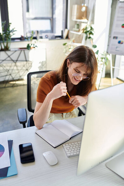 В современном офисе молодой небинарный человек улыбается, усердно работая над задачами.