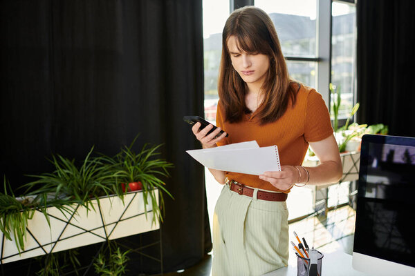 A young non binary person multitasks, studying papers while checking their phone.