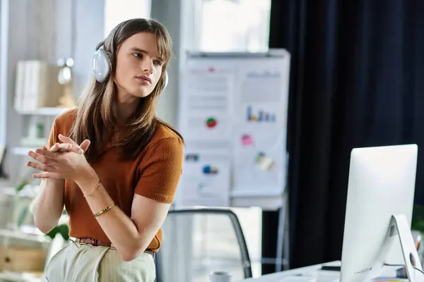 stock image A young non binary person listens intently while working at their desk in an office.