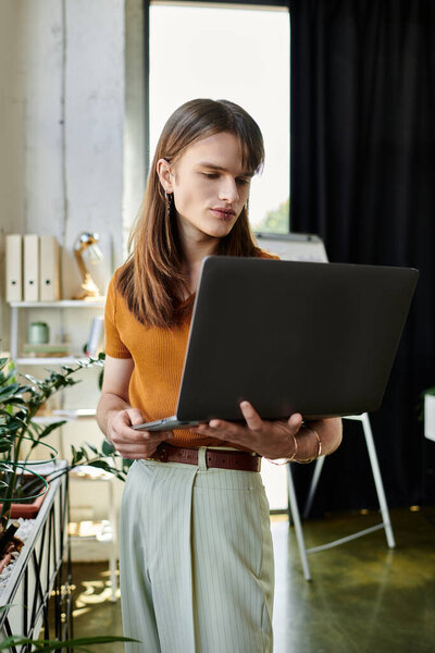 In a cozy office, a young non binary person works intently on their laptop amid plants.