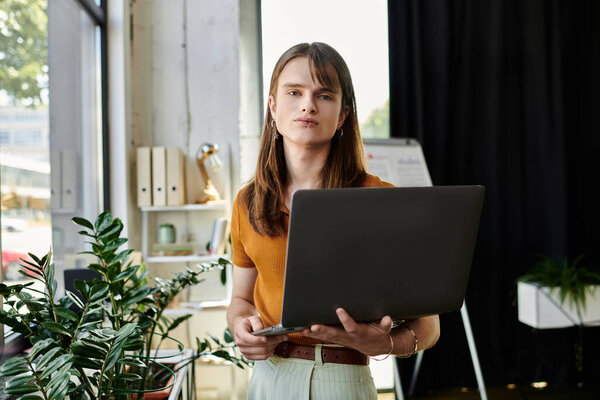 A young non binary individual is focused on a laptop, surrounded by greenery in a vibrant office.