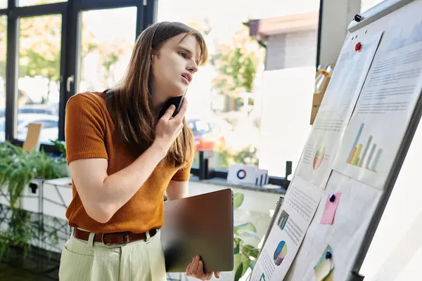 stock image In a vibrant workspace, a non binary person reflects on charts while holding a tablet.