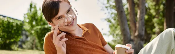 stock image A non binary individual relaxes in an office, sipping coffee and smiling, exuding creativity.