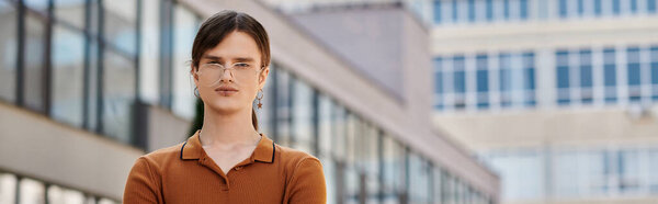 Молодой небинарный человек уверенно позирует в офисе.