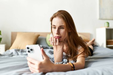 Genç bir kadın, telefonuyla uğraşırken derin düşünceler içinde yatağında dinleniyor..