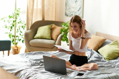 Genç bir kadın dizüstü bilgisayarıyla uğraşırken mutluluk saçıyor, rahat ev konforlarıyla çevrili..