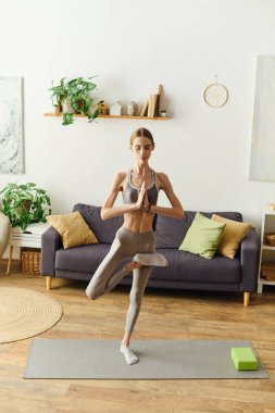 Konforlu bir oturma odasında anoreksisi olan genç bir kadın yoga yapıyor. Zindelik ve sağlığa olan bağlılığını somutlaştırıyor..