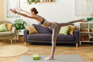Konforlu bir oturma odasında, anoreksisi olan genç bir kadın spor salonuna odaklanırken yoga pozu verir..