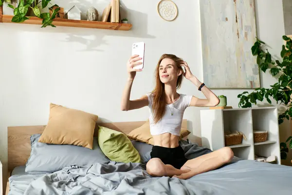 stock image A young woman sits cross-legged on her bed, taking a moment to capture her thoughts surrounded by a calm atmosphere.