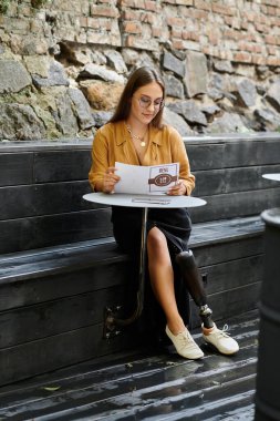 Kafe masasında oturan genç bir kadın menüyü okuyor ve protez bacağını stille sergiliyor..