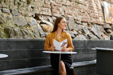 Şık bir kafede, protez bacaklı genç bir kadın küçük bir masada rahatça oturur ve menüyle ilgilenir..