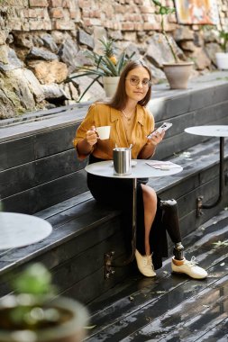 Protez bacaklı genç bir kadın bir kafede oturur, kahvesini yudumlar ve telefonunu kontrol eder, gününün tadını çıkarır..