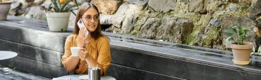 Genç bir kadın kahve yudumluyor ve büyüleyici bir kafede telefonuyla sohbet ediyor.