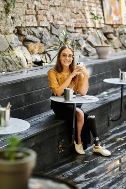 Protez bacaklı genç bir kadın bir kafede rahatça oturur, içkisini yudumlar ve hayattan zevk alır..