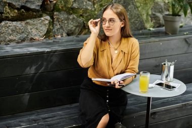 Canlı bir kafede, protez bacaklı genç bir kadın defterine odaklanıp günlük yaşamını yakalarken bir şeyler içmekten zevk alıyor..