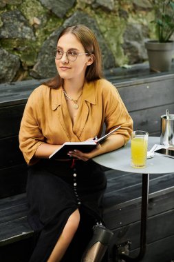 In a cozy cafe, a young woman with a prosthetic leg thoughtfully writes in her notebook, embodying a vibrant lifestyle. clipart