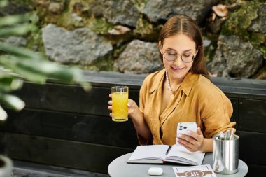 Protez bacaklı genç bir kadın bir kafede rahatlıyor, telefonuna ve defterine odaklanırken bir yudum içki içiyor..