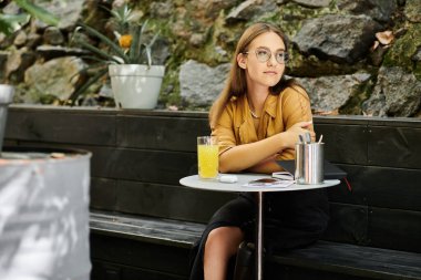 Genç bir kadın bir kafe masasında rahatlar, içkisinin tadını çıkarırken aynı zamanda protez bacağını sergiler, dayanıklılığını somutlaştırır..